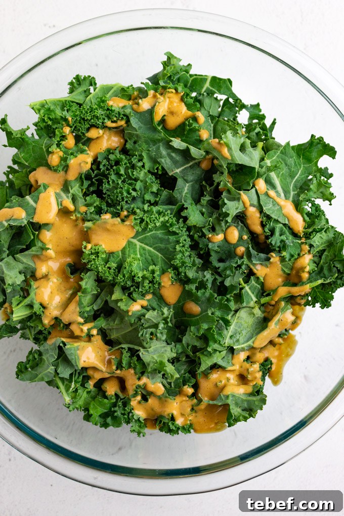 Thai Kale Salad with Creamy Peanut Dressing 5 kale leaves in a mixing bowl with some of the peanut dressing over top.