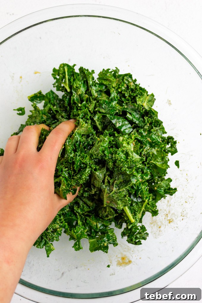 Thai Kale Salad with Creamy Peanut Dressing 6 kale in a mixing bowl with a hand massaging it.