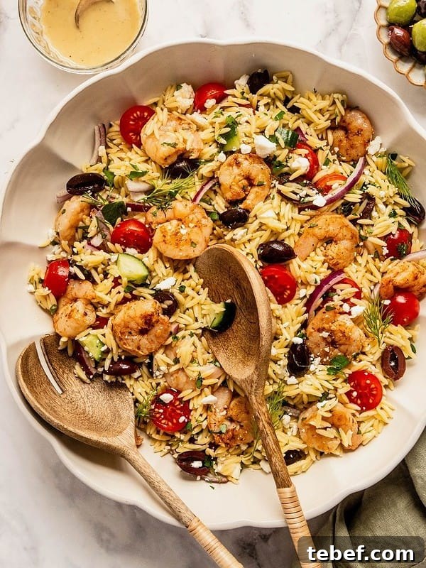 Mediterranean orzo salad with shrimp, olives, tomatoes, cucumbers and sliced onions in a bowl.