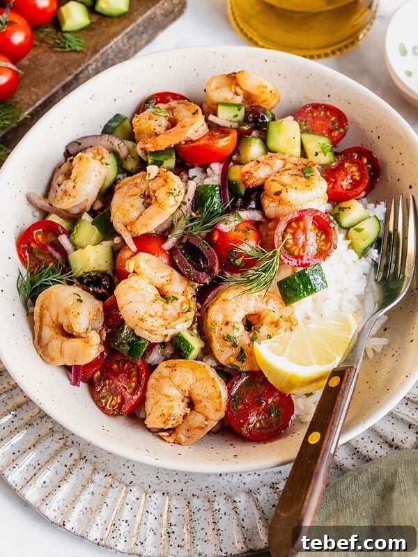 Mediterranean shrimp rice bowl with chopped cucumber, tomatoes, olives garnished with fresh dill.