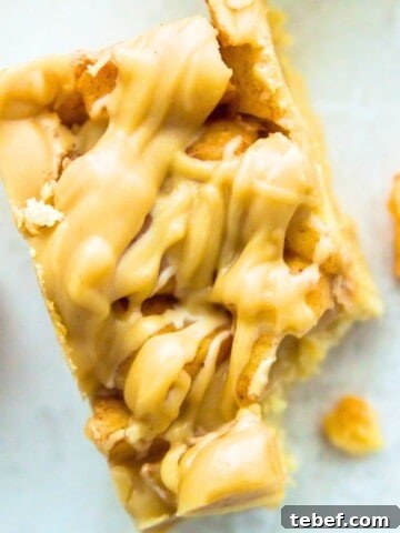 A paleo apple pie bar with a bite out of it and pieces of cooked apples beside it.