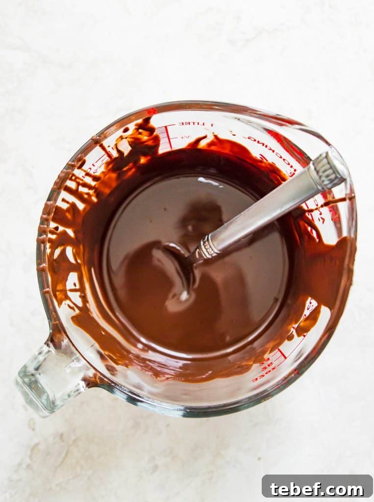 Vegan Hot Chocolate Bombs: Dairy-Free Paleo Recipe and How-To 3 A glass measuring cup full of melted chocolate with a spoon in it.