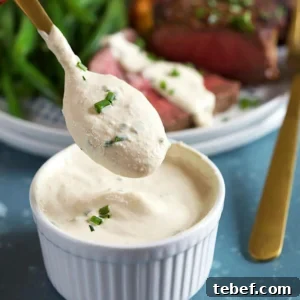 Creamy Horseradish Sauce Recipe: Smooth, Tangy & Versatile 7 Creamy Horseradish Sauce on a gold spoon over a bowl of horseradish sauce on a blue background.