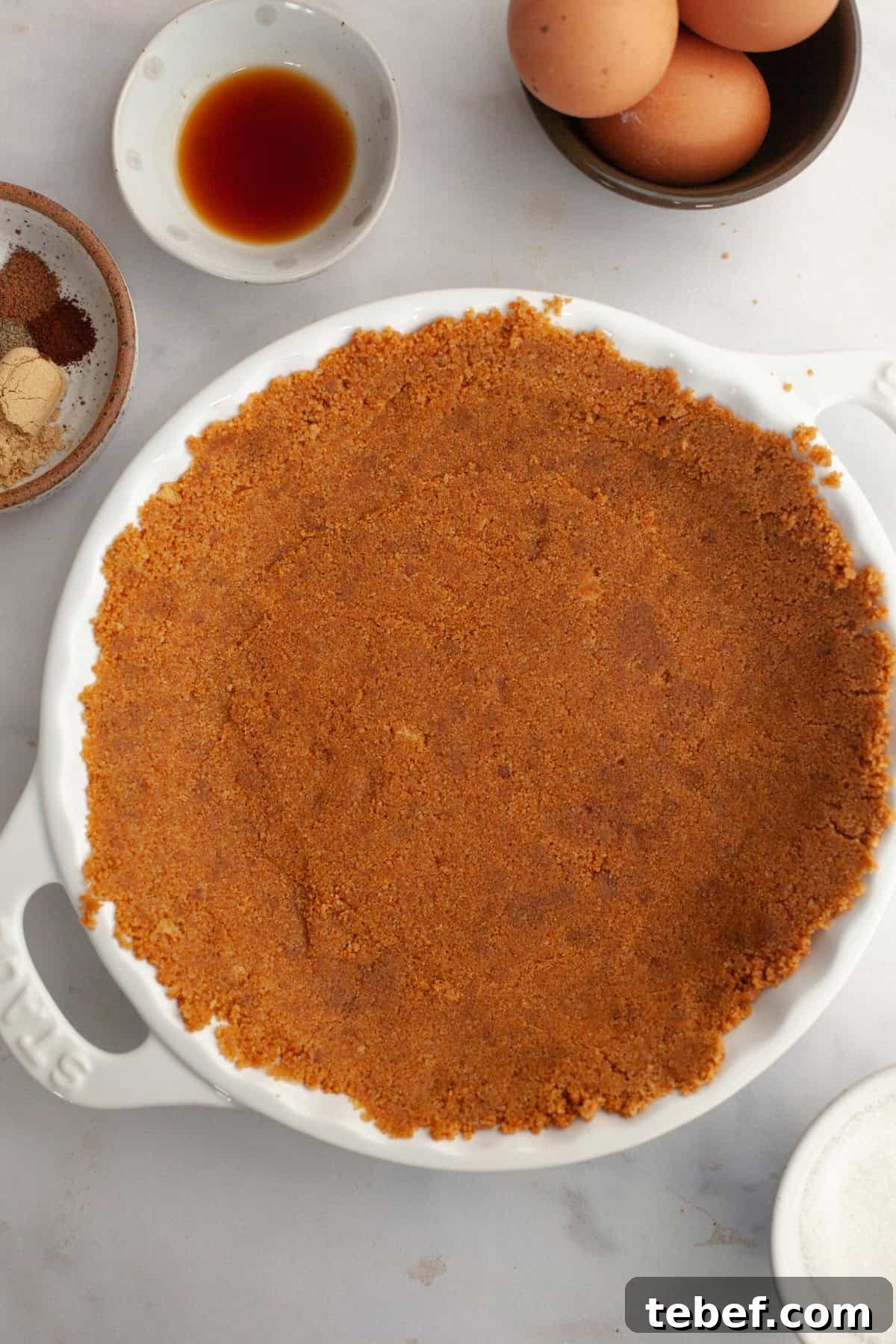 A white ceramic pie dish with a gingersnap crust in it.