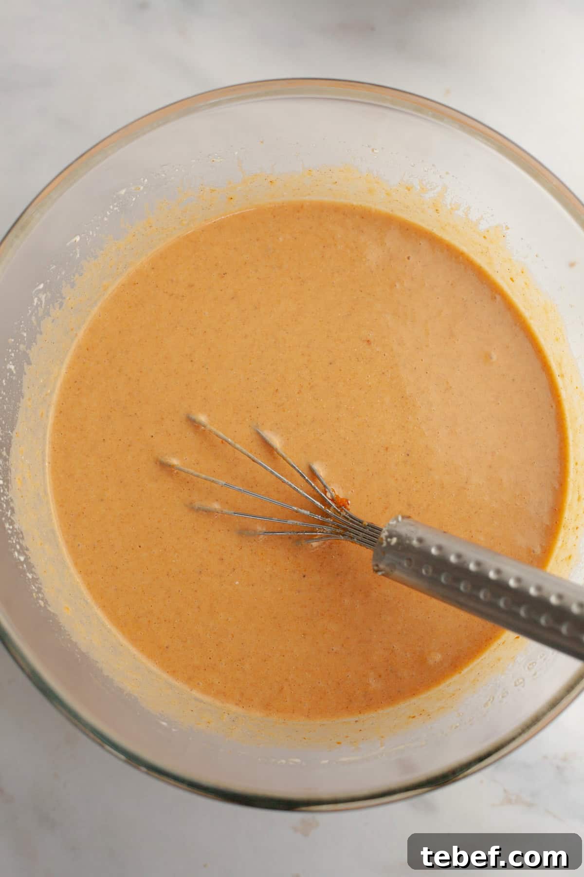 Pumpkin pie filling in a glass bowl with a whisk.