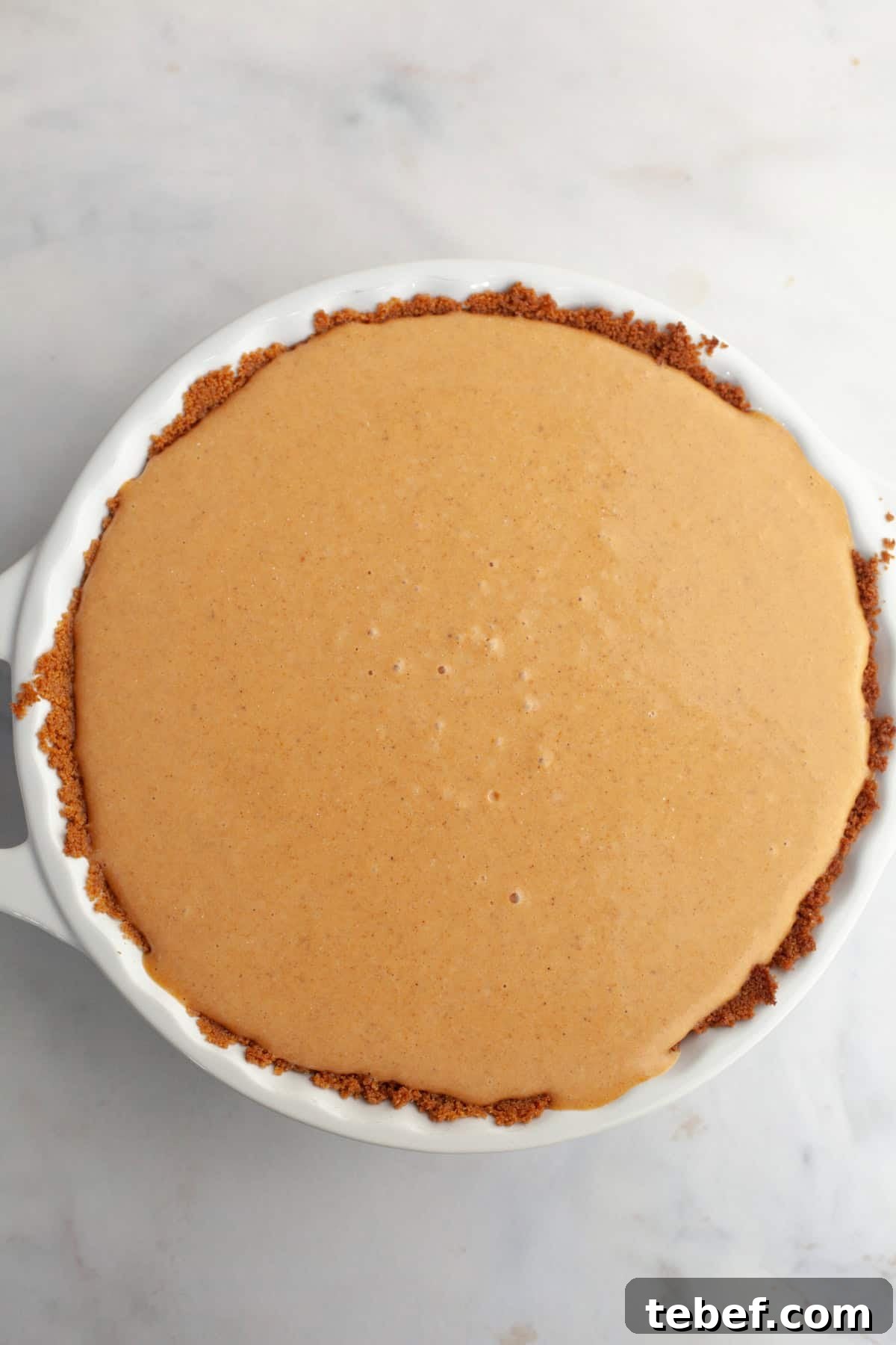 An unbaked pumpkin pie in a white ceramic baking dish.