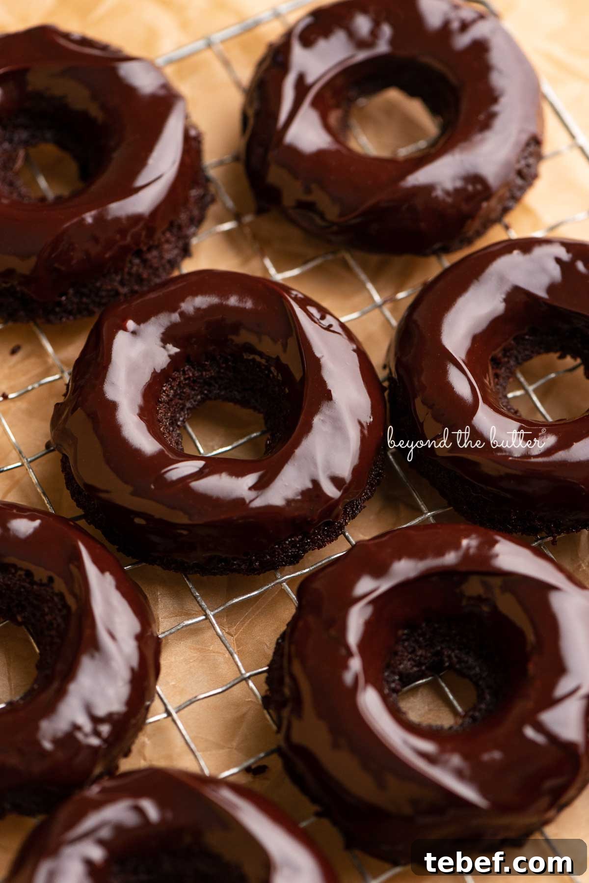 Homemade Baked Chocolate Donuts Recipe for Moist, Rich Donuts 4 Homemade baked chocolate donuts topped with chocolate ganache on a wire cooling rack | © Beyond the Butter®