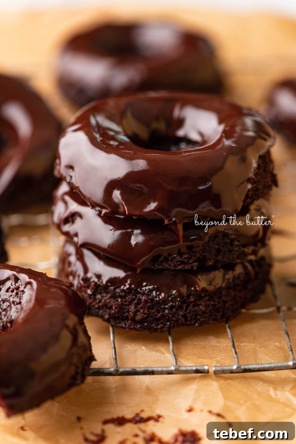 Homemade Baked Chocolate Donuts Recipe for Moist, Rich Donuts 5 Stacked homemade baked chocolate donuts topped with chocolate ganache on a wire cooling rack | © Beyond the Butter®