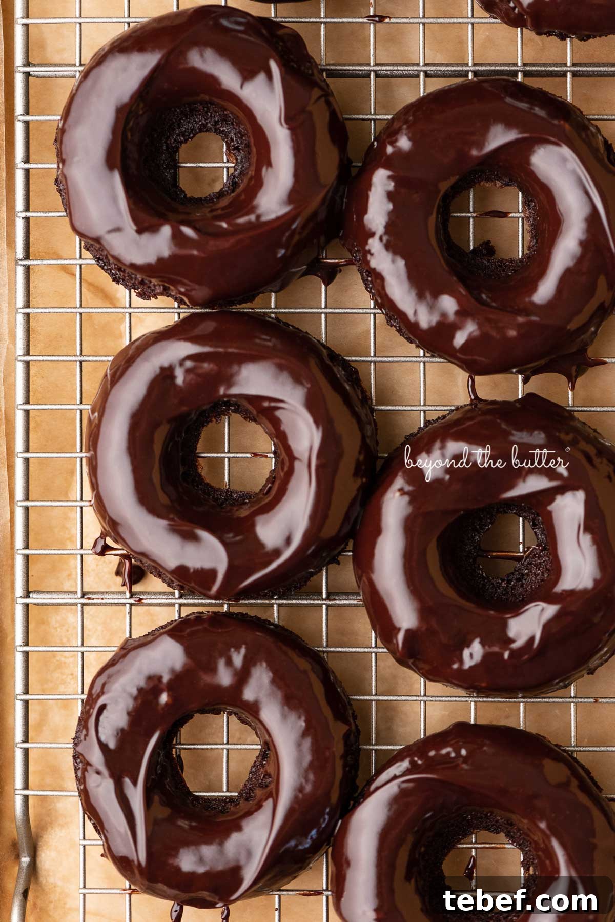 Homemade Baked Chocolate Donuts Recipe for Moist, Rich Donuts 6 Homemade baked chocolate donuts topped with chocolate ganache on a wire cooling rack | © Beyond the Butter®