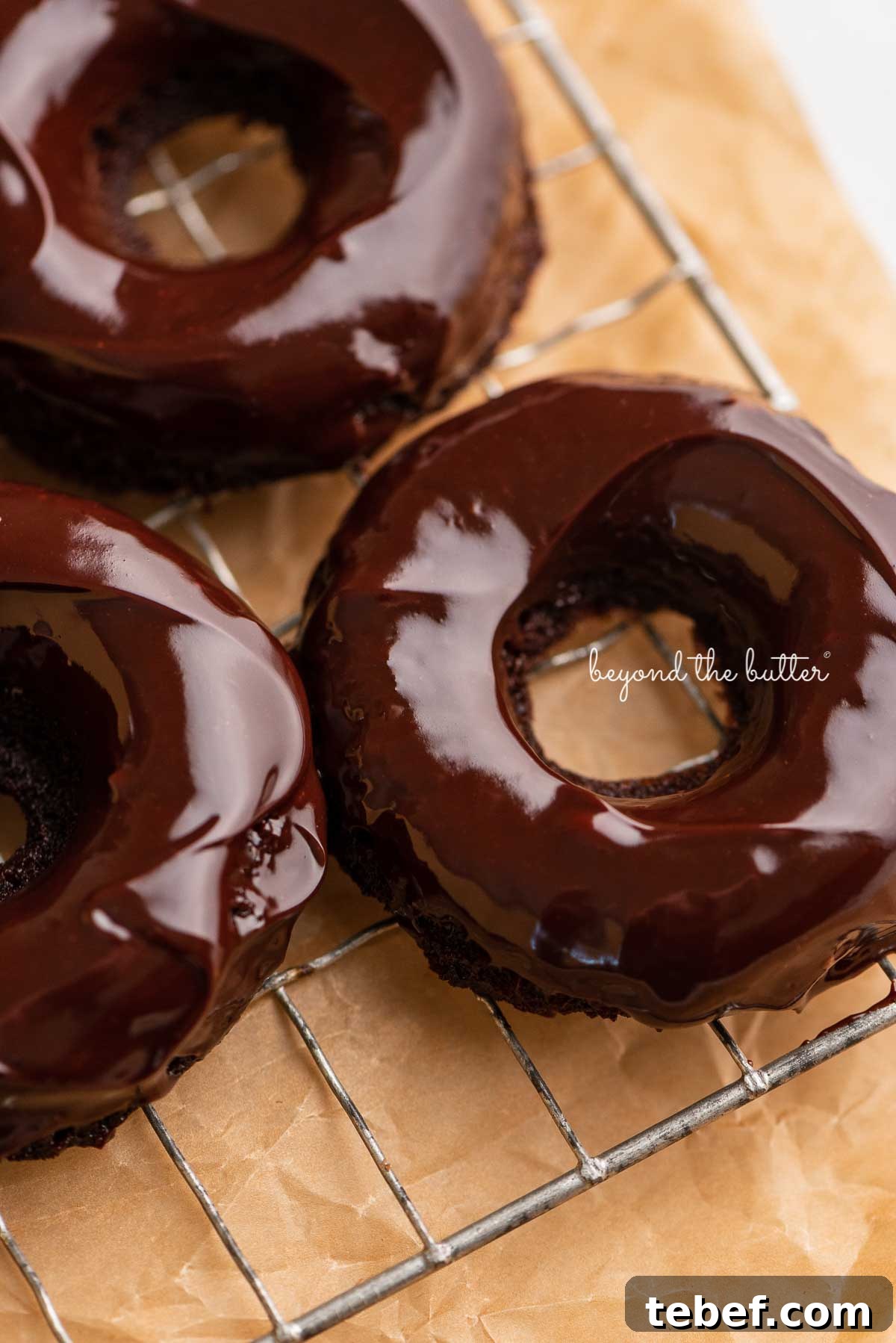 Homemade Baked Chocolate Donuts Recipe for Moist, Rich Donuts 7 Homemade baked chocolate donuts topped with chocolate ganache on a wire cooling rack | © Beyond the Butter®