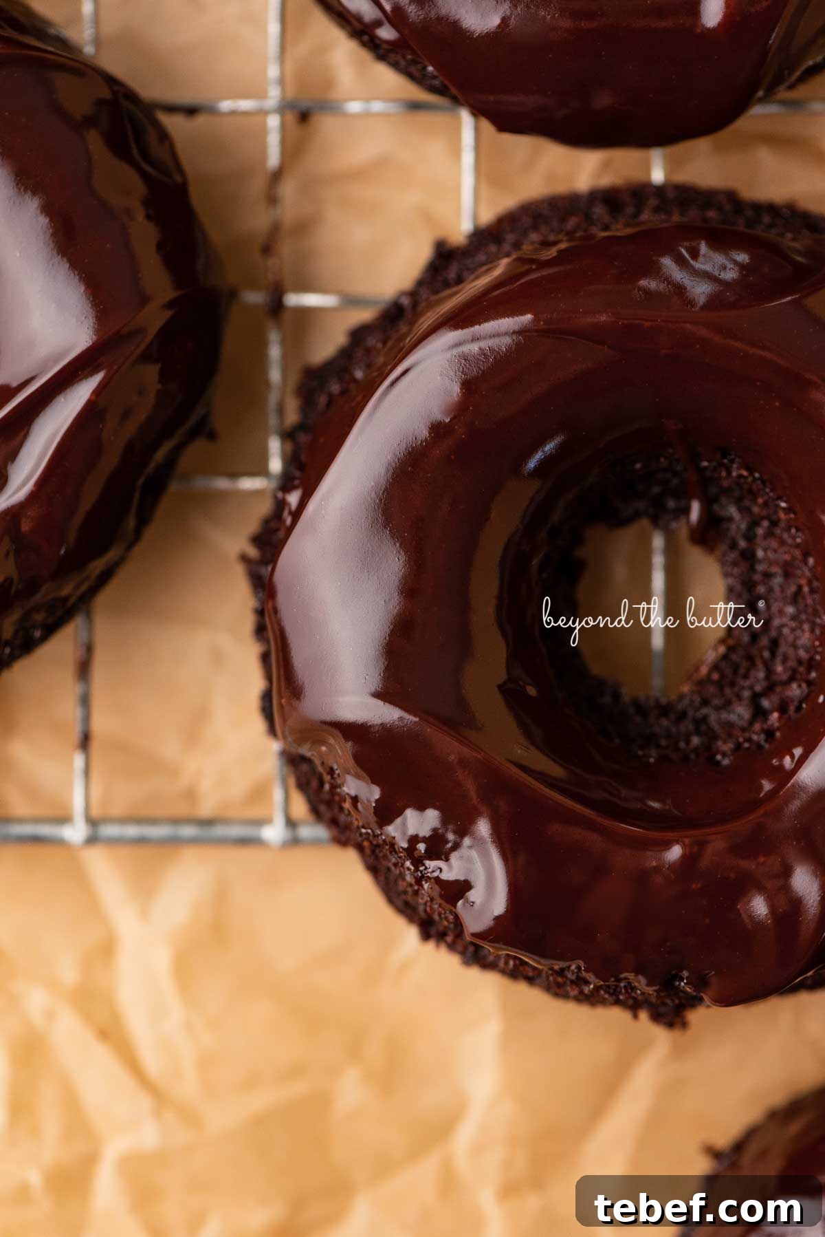 Homemade Baked Chocolate Donuts Recipe for Moist, Rich Donuts 8 Close up of homemade baked chocolate donuts topped with chocolate ganache on a wire cooling rack | © Beyond the Butter®