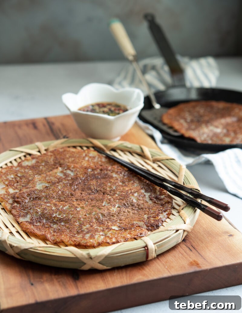 Crispy Korean Potato Pancakes (Gamja-Jeon) — Authentic Recipe 12 Golden crispy Korean potato pancakes served on a woven plate with chopsticks and soy chili dipping sauce