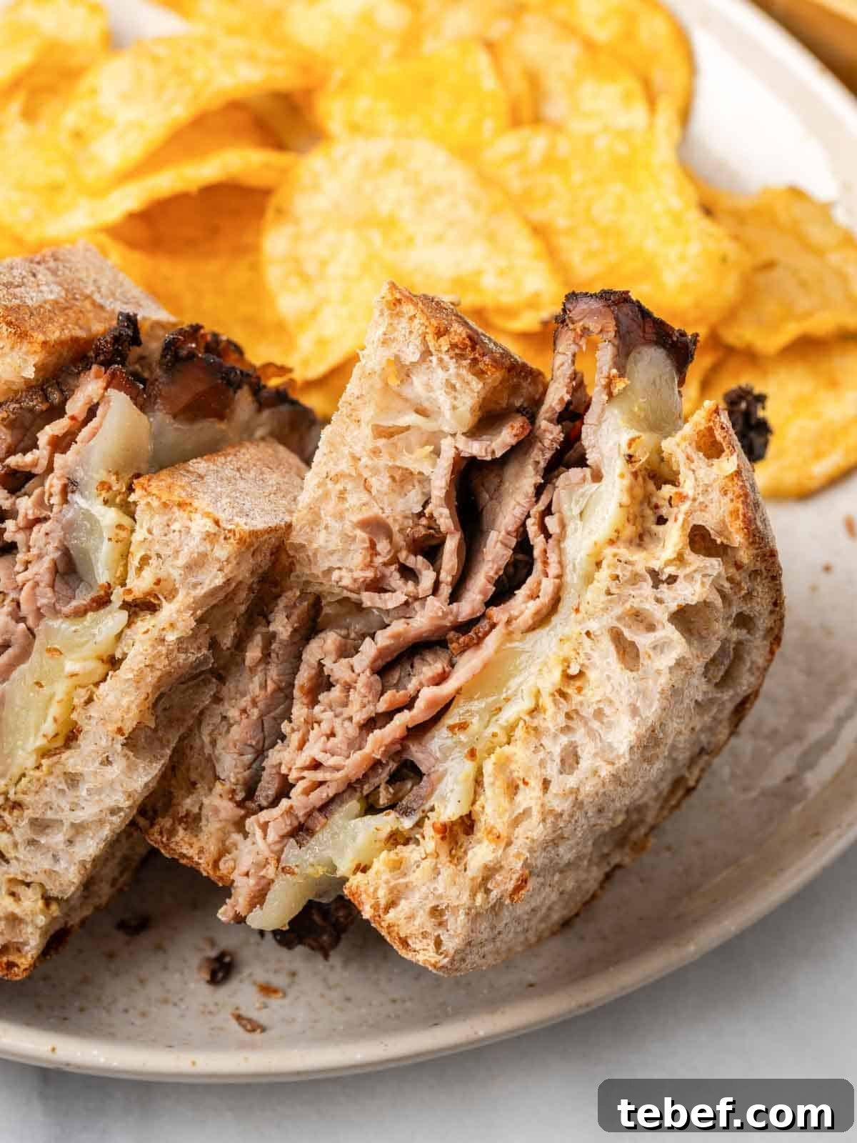 roast beef sandwich halves on plate with chips.