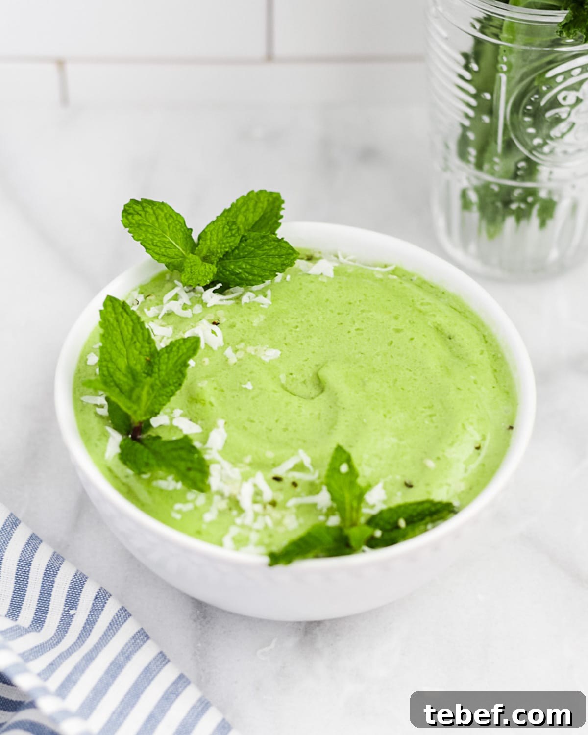 A 45 degree angle shot of a smoothie in a white bowl. Garnished with mint and coconut flakes.