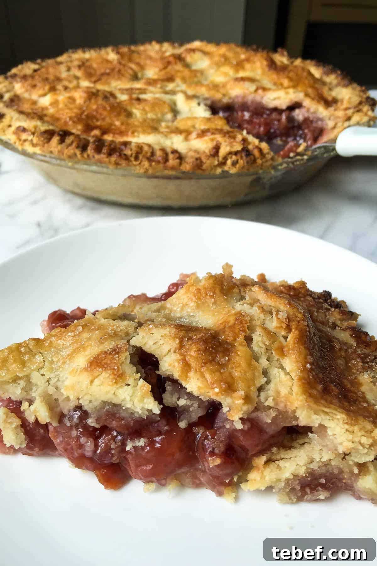 Classic Homemade Cherry Pie Recipe with Flaky Crust 2 Piece on white plate with whole pie in background.