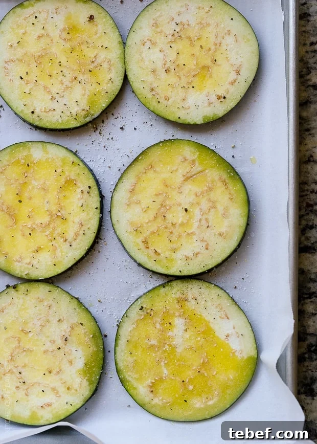 Slices of eggplant on a sheet pan, ready to roast in the oven.