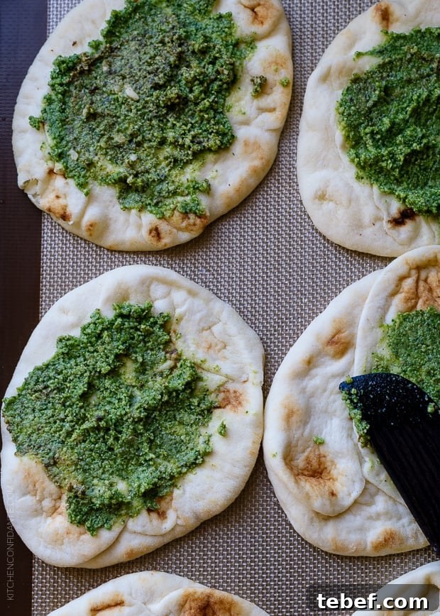 Mini naan spread with pesto on a baking sheet.