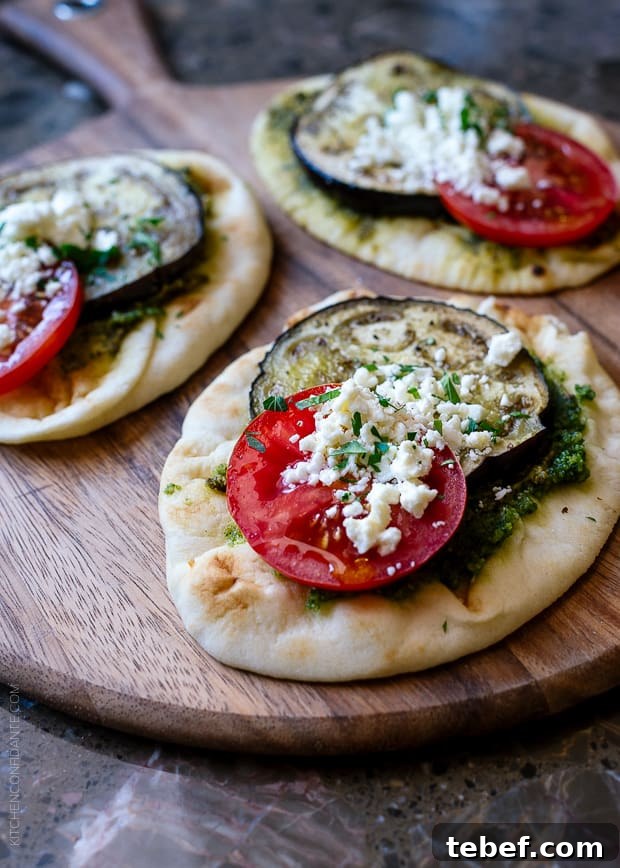 Mini naan topped with roasted vegetables on a wooden surface.
