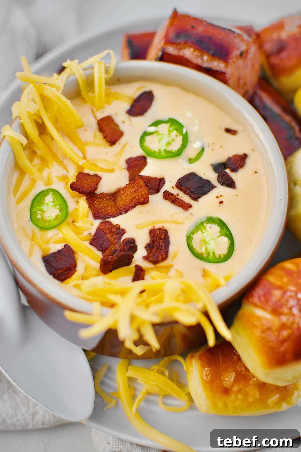 Creamy Beer Cheese Soup Recipe with Bacon and Pretzel Croutons 2 Beer Cheese Soup topped with more cheese, bacon bits, and serrano chili slices, ready to eat. Served with Kielbasa and Pretzel Bites