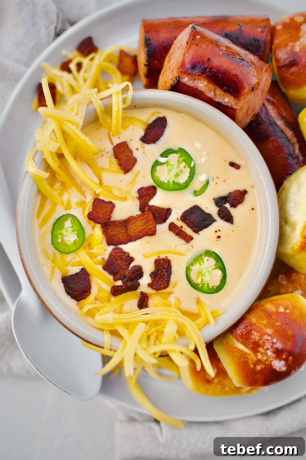 Creamy Beer Cheese Soup Recipe with Bacon and Pretzel Croutons 12 Beer Cheese Soup topped with more cheese, bacon bits, and serrano chili slices, ready to eat. Served with Kielbasa and Pretzel Bites