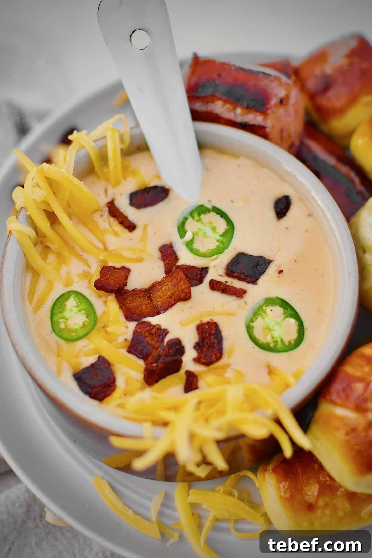 Creamy Beer Cheese Soup Recipe with Bacon and Pretzel Croutons 13 Beer Cheese Soup topped with more cheese, bacon bits, and serrano chili slices, ready to eat. Served with Kielbasa and Pretzel Bites