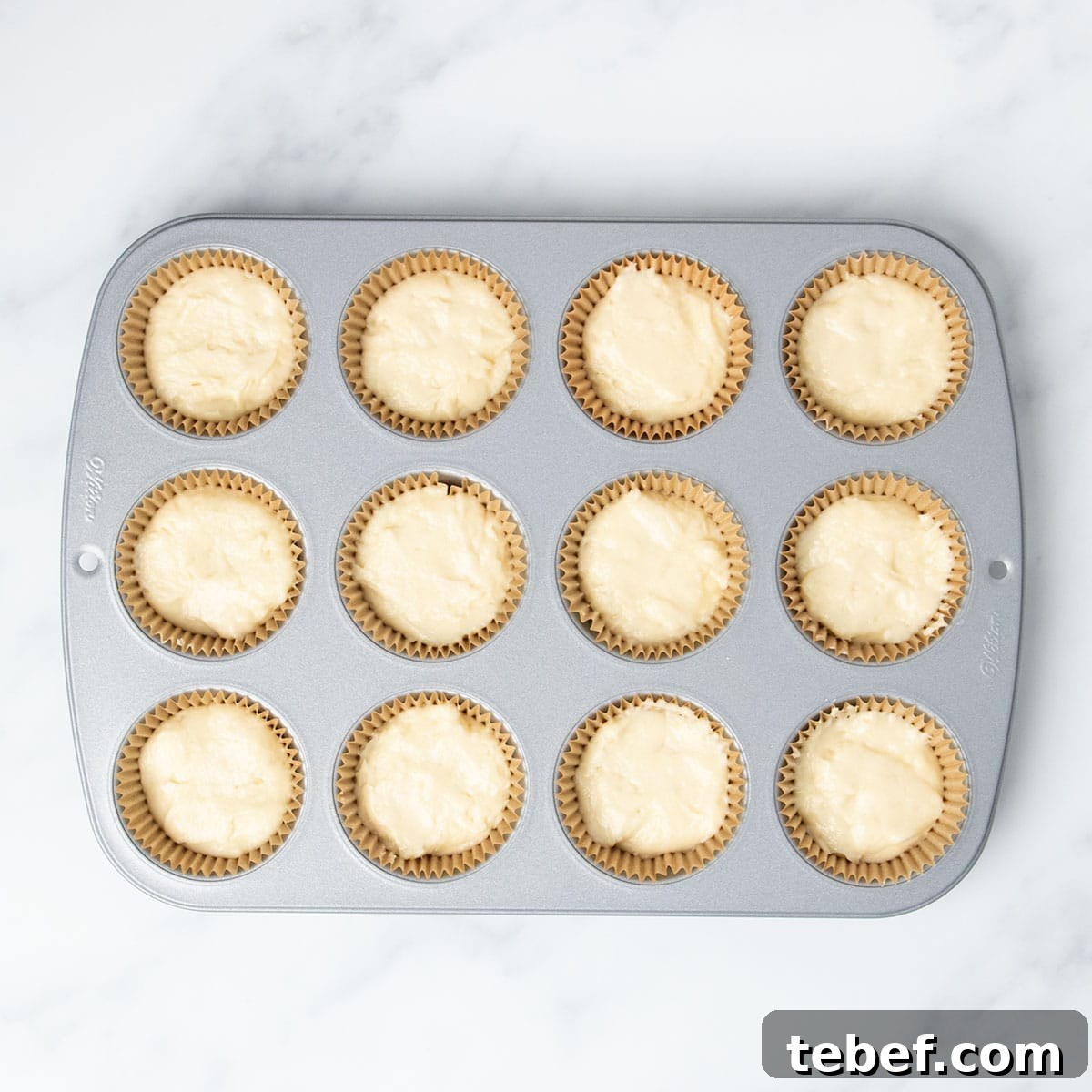 Gluten-Free Vanilla Cupcakes Recipe for Moist, Fluffy Results 13 standard 12 cup metal muffin tin with brown muffin liners in wells filled 2/3 of the way full with light yellow raw cupcake batter