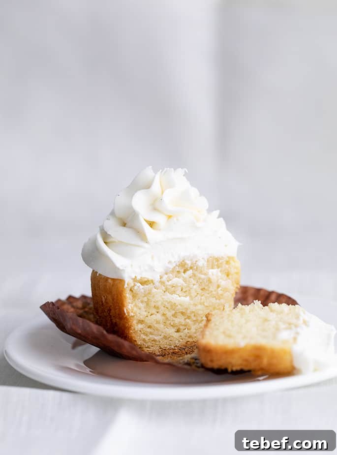 Gluten-Free Vanilla Cupcakes Recipe for Moist, Fluffy Results 3 One gluten free vanilla cupcake with swirled white frosting cut in two pieces on brown paper liner on a small white plate above a white cloth