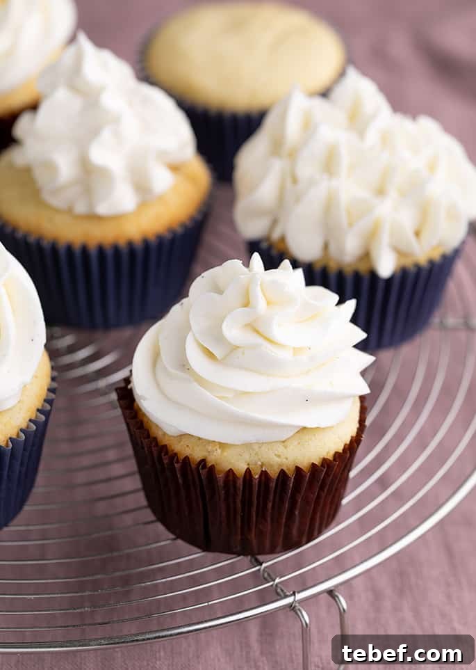 Gluten-Free Vanilla Cupcakes Recipe for Moist, Fluffy Results 5 Yellow cupcakes with frosting in paper liners on round wire rack above purple cloth