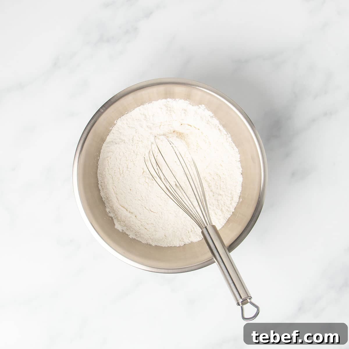Gluten-Free Vanilla Cupcakes Recipe for Moist, Fluffy Results 6 small round metal mixing bowl with whisked white powder and wire whisk