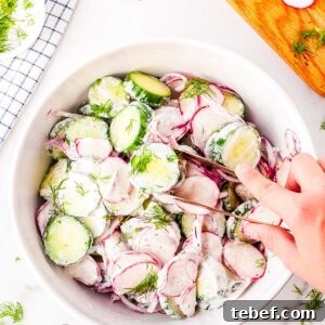 A hand with tongs int he picking up some of the cucumber and radish salad from a serving bowl.