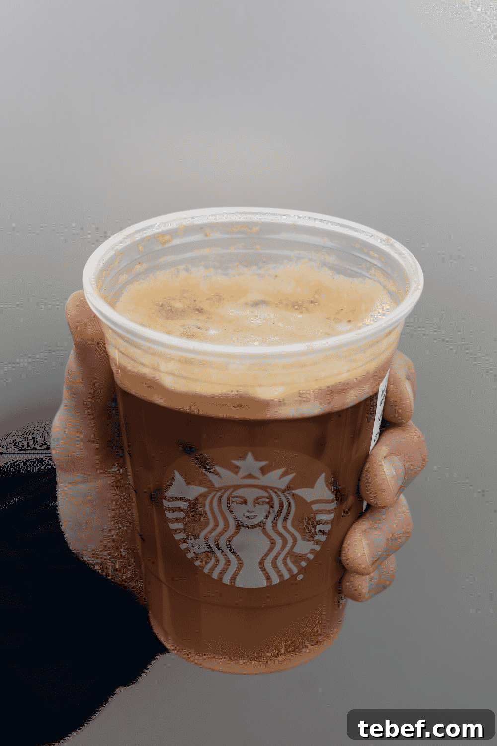 A hand holding a cup of Starbucks vegan iced shaken espresso.