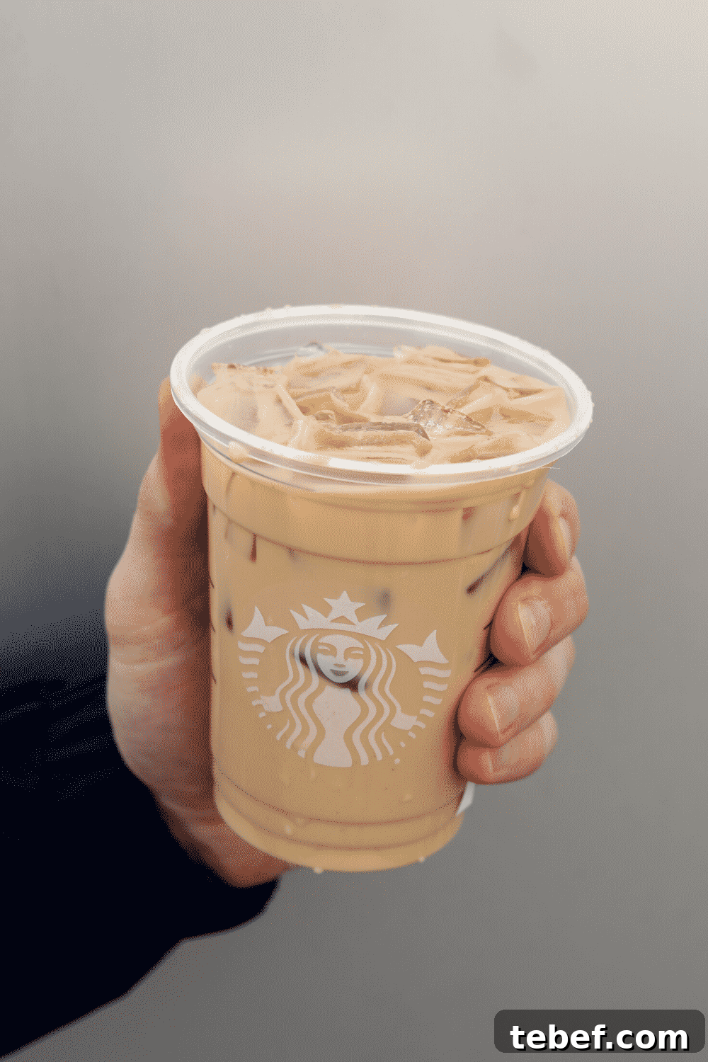 A hand holding a cup of Starbucks vegan iced cinnamon dolce latte.