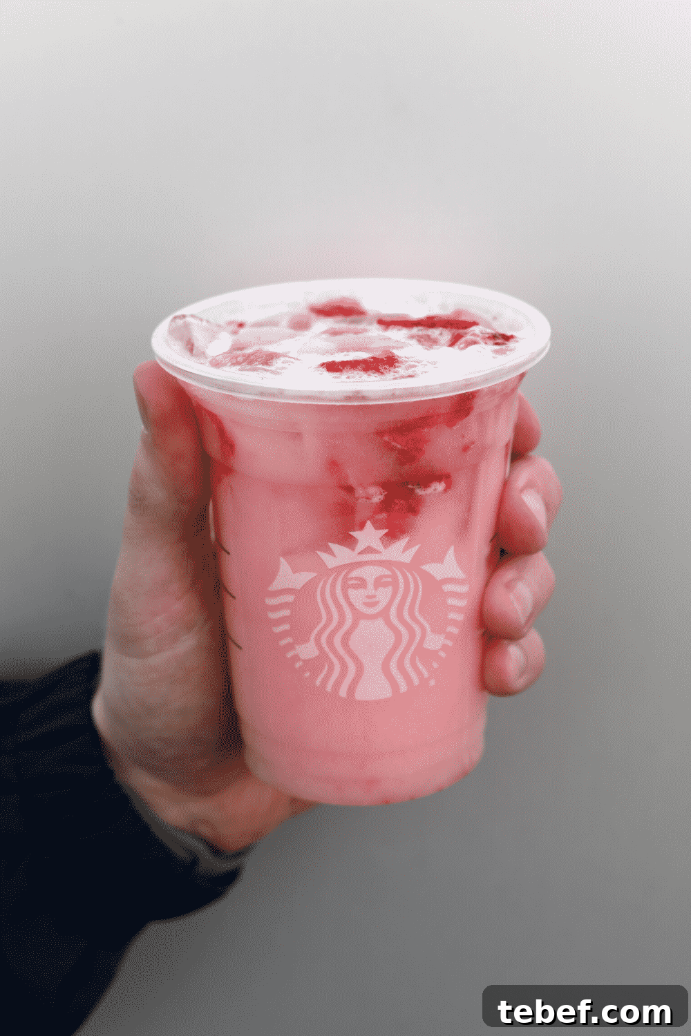 A hand holding a cup of Starbucks vegan pink drink.