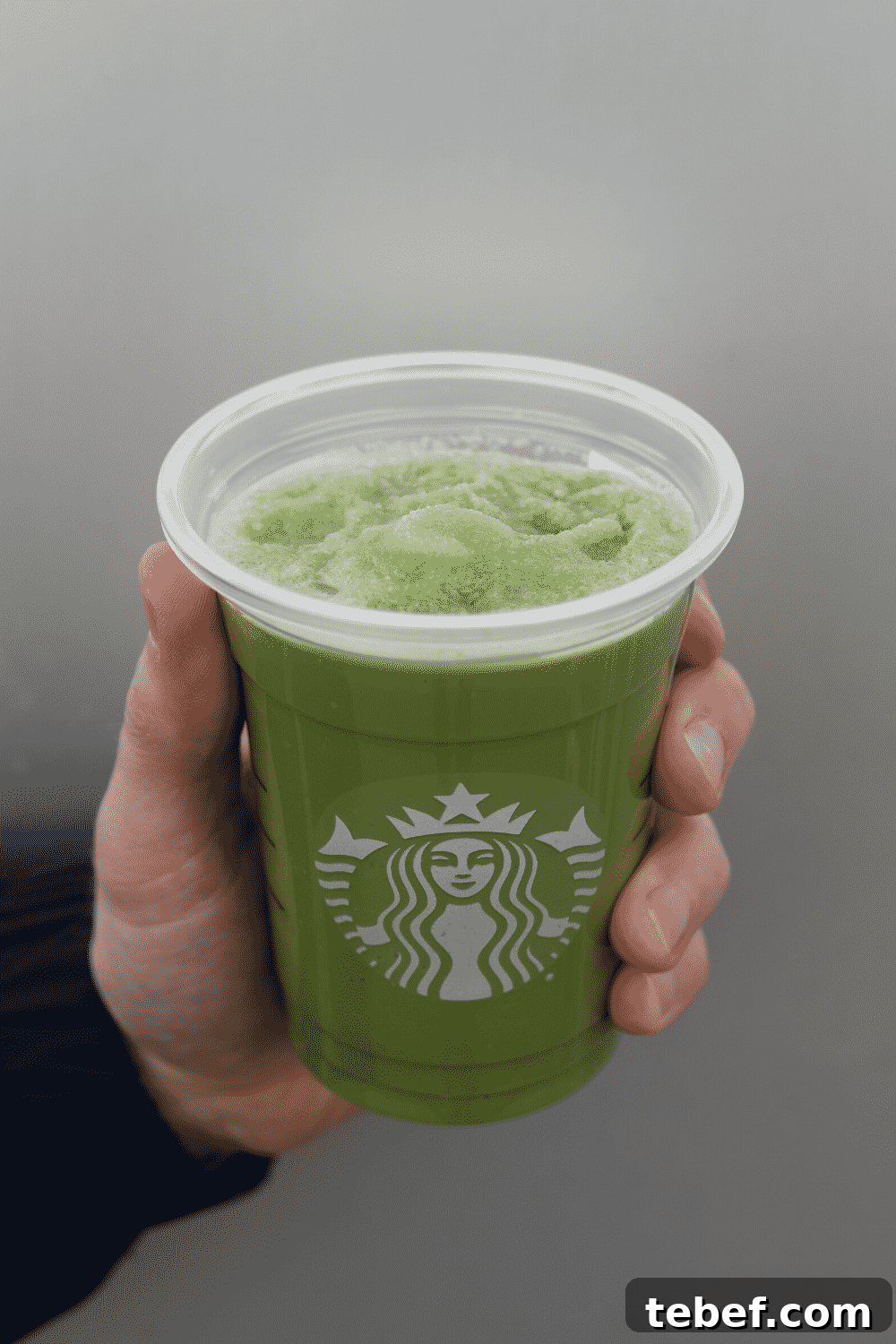 A hand holding a cup of Starbucks vegan macha green tea creme Frappuccino