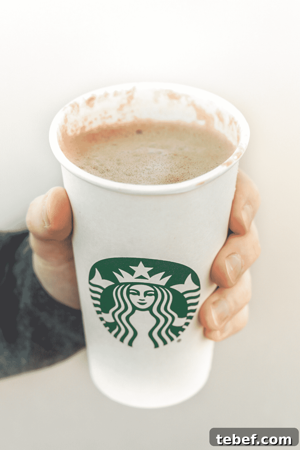 A hand holding a cup of Starbucks vegan café blonde vanilla latteA hand holding Starbucks vegan caffe blonde vanilla latte