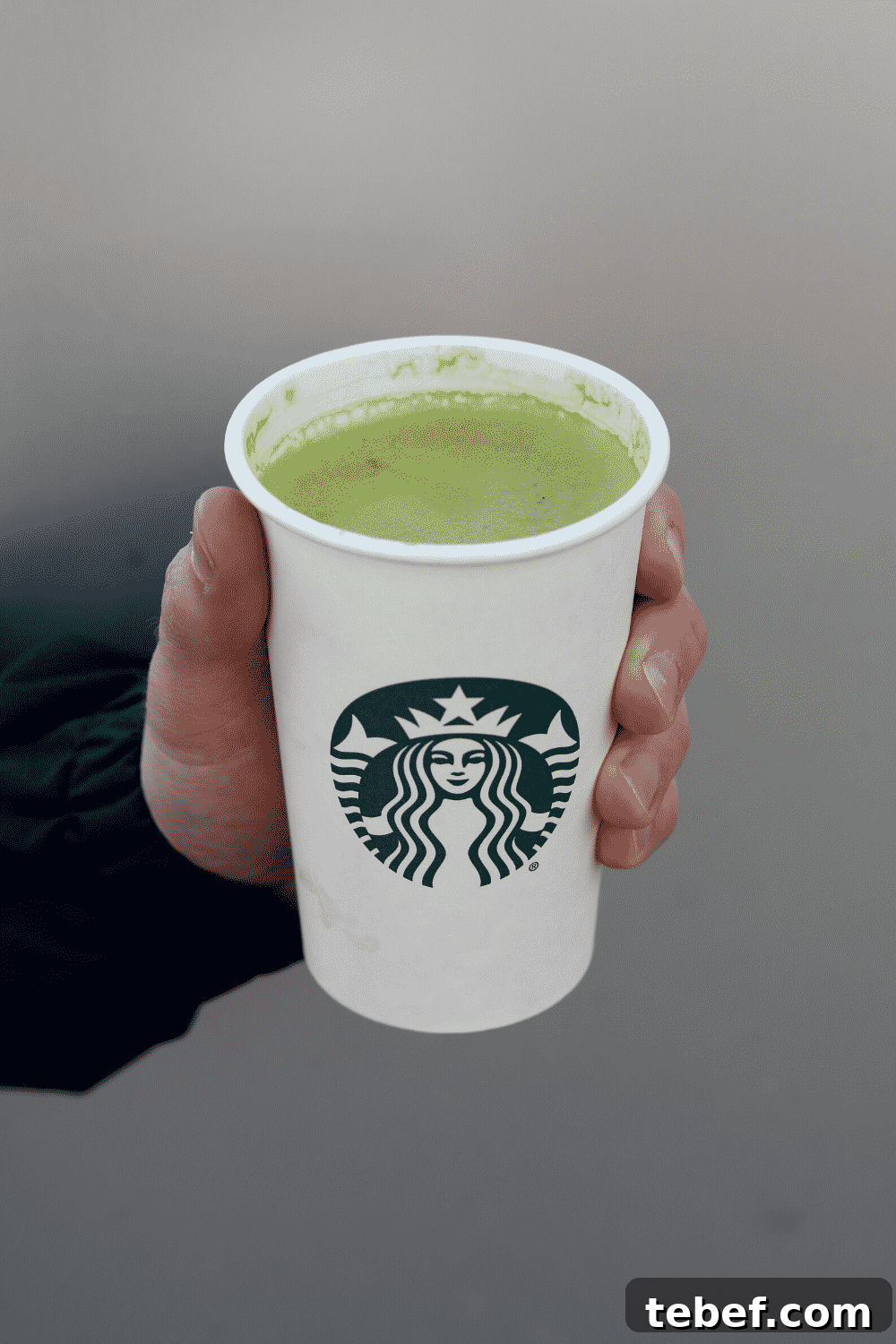 A hand holding a cup of Starbucks vegan Matcha green tea latte.