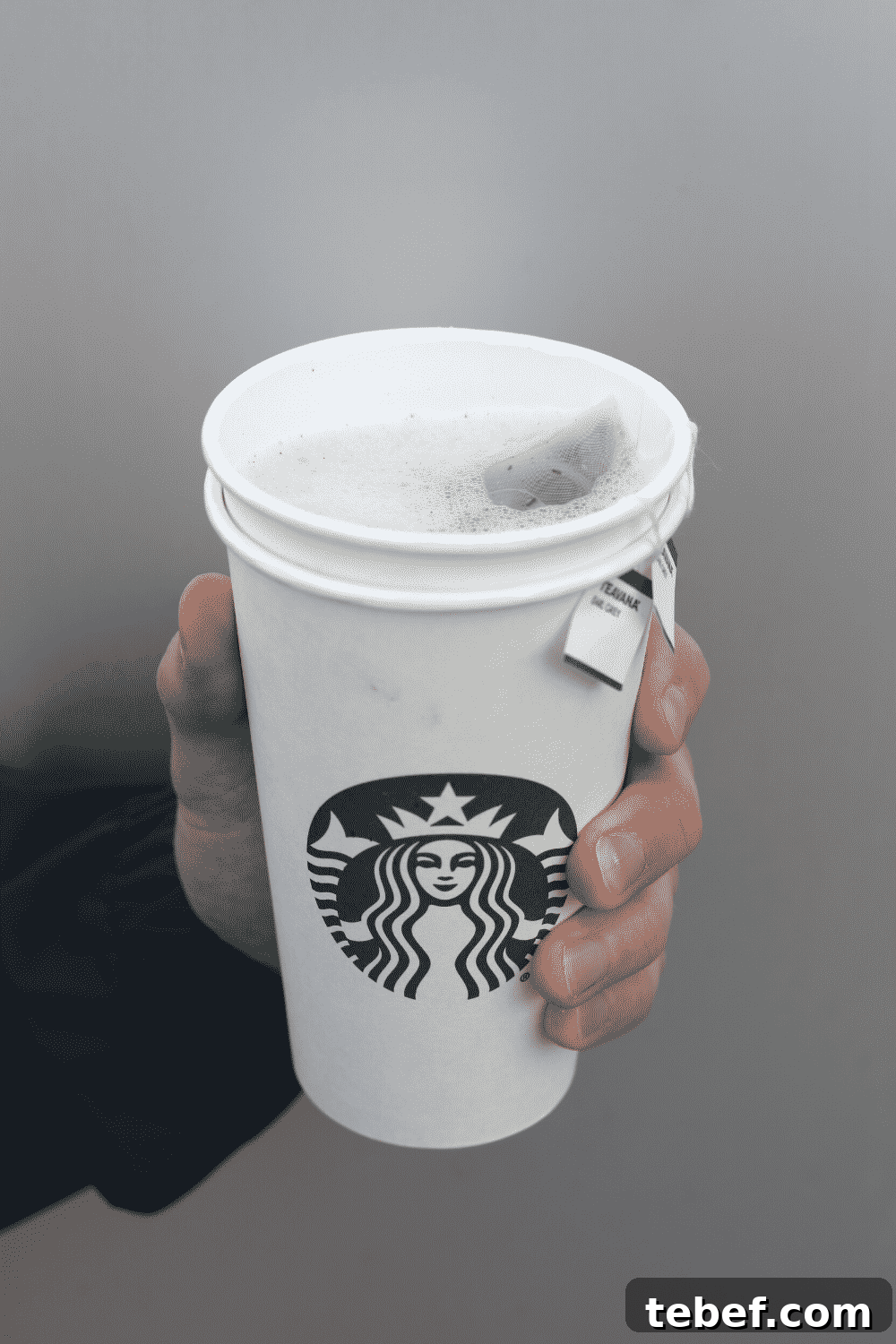 A hand holding a cup of Starbucks vegan London fog tea latte.