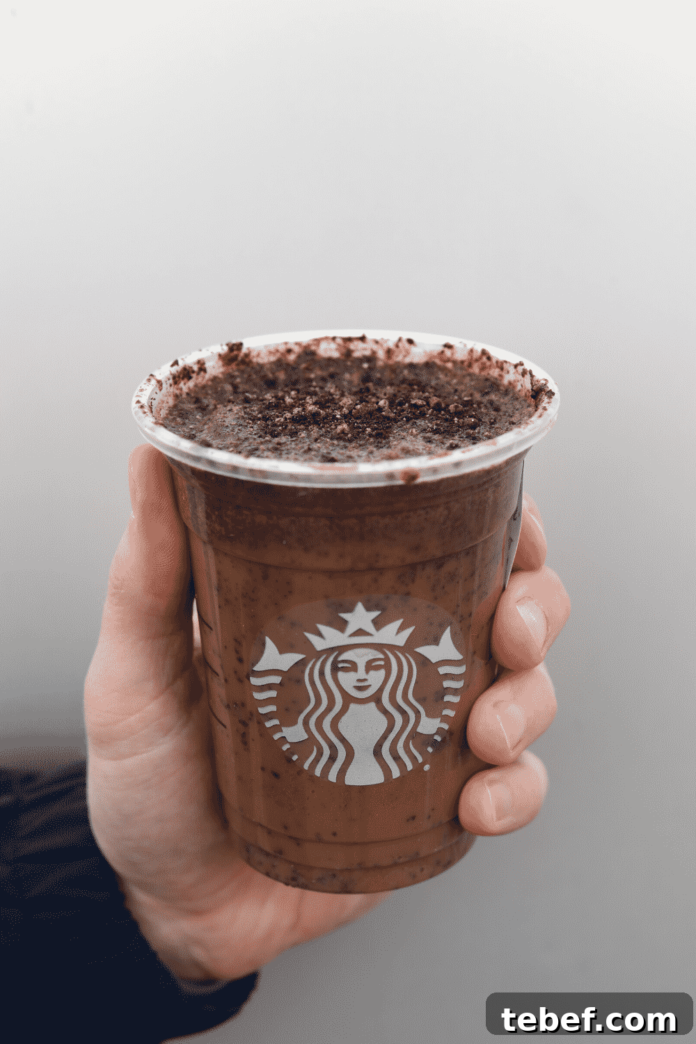 A hand holding a cup of Starbucks vegan mocha cookie crumble Frappuccino.