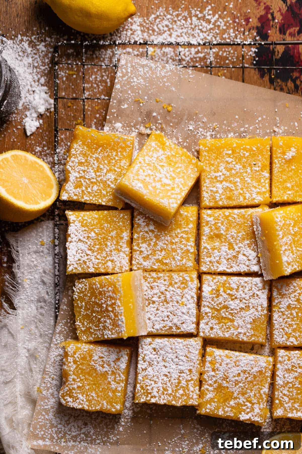 Zesty Lemon Bars with Buttery Shortbread Crust 9 Lemon bars cut into squares and dusted with powdered sugar on brown parchment paper.
