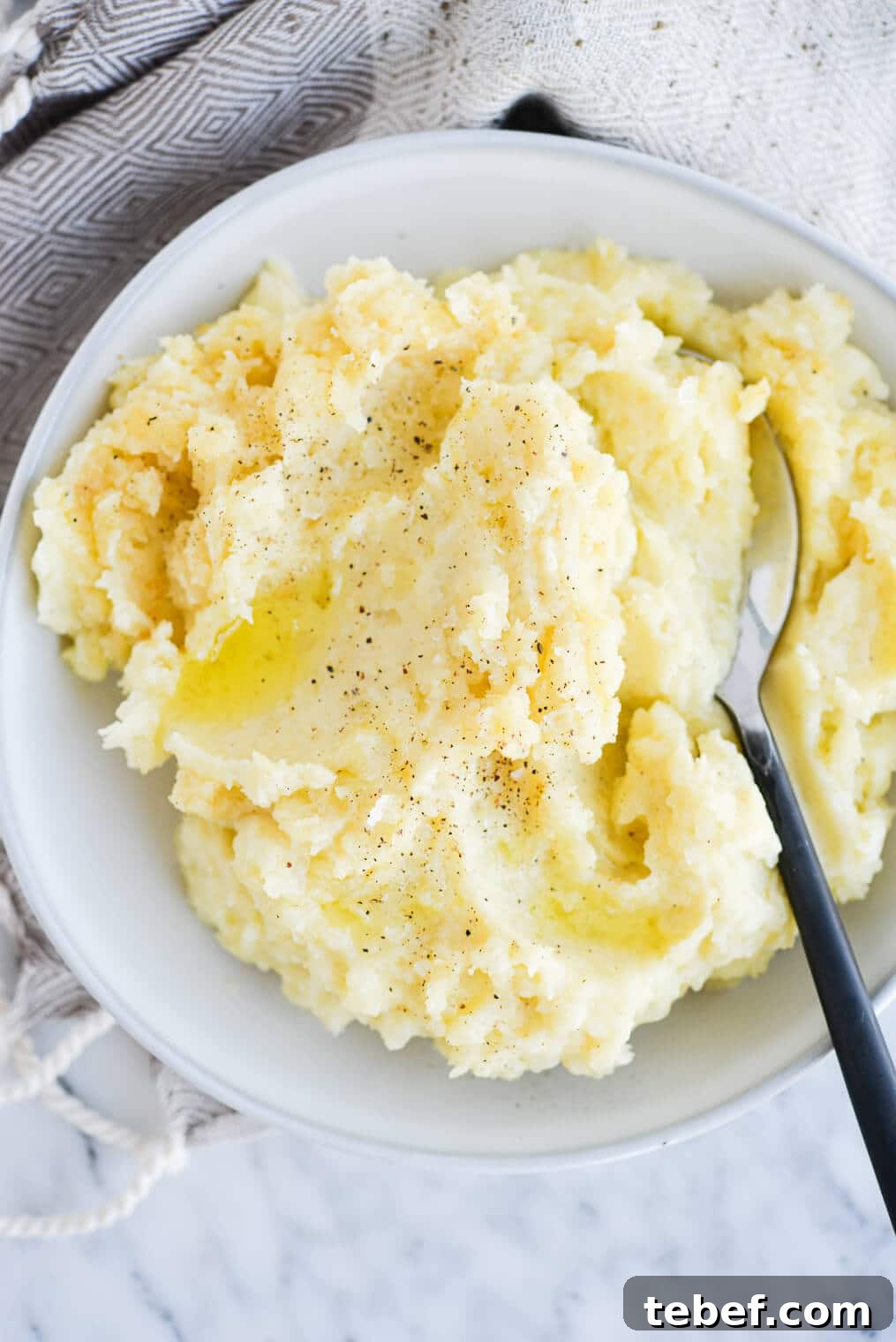 Ultra-Creamy Mashed Potatoes Recipe for Perfect Texture 2 top view of a bowl of ready-to-eat mashed potatoes with a serving spoon sitting on a marble surface