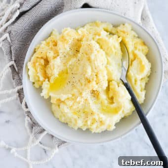 Ultra-Creamy Mashed Potatoes Recipe for Perfect Texture 14 top view of a bowl of ready-to-eat mashed potatoes with a serving spoon sitting on a marble surface