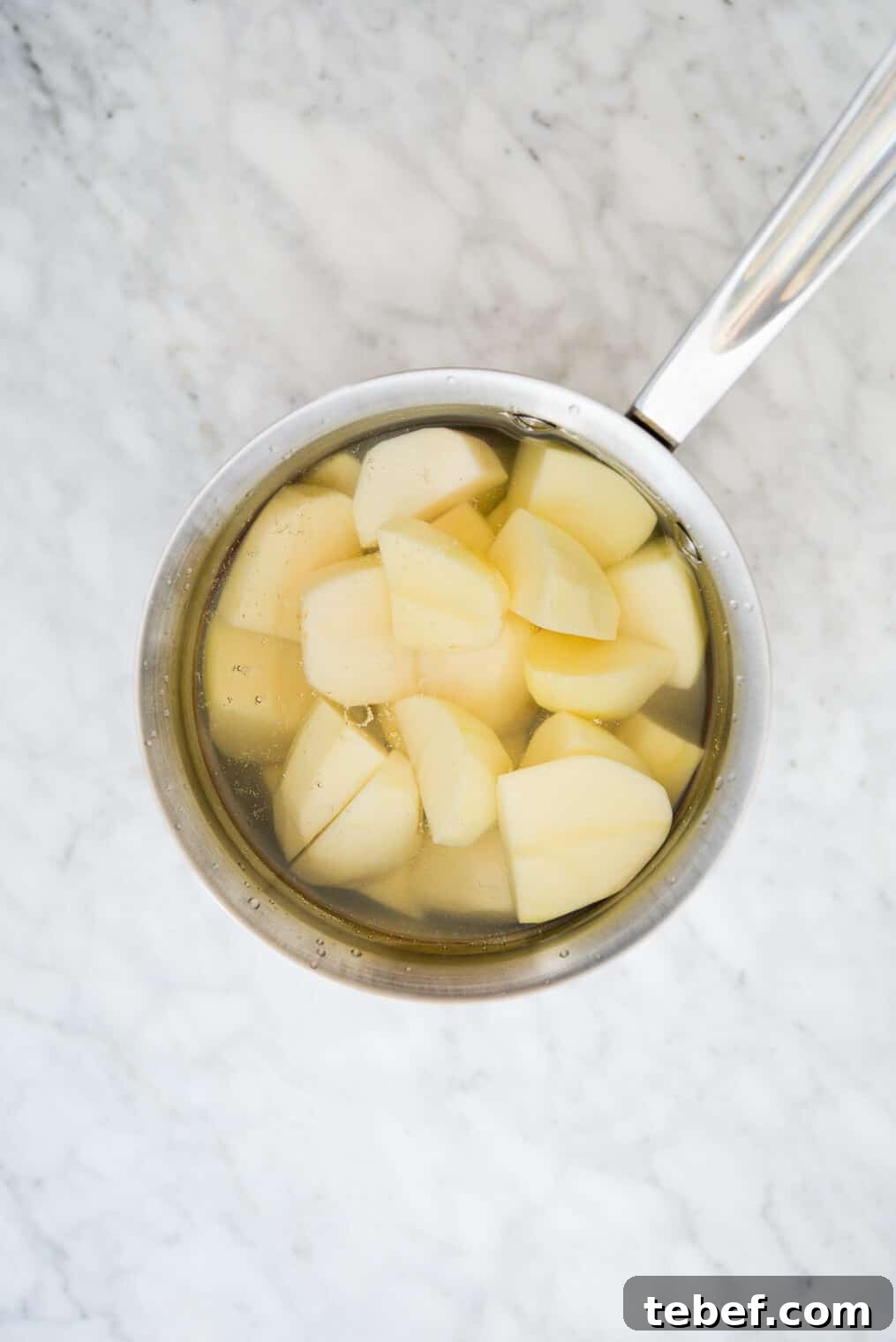 Ultra-Creamy Mashed Potatoes Recipe for Perfect Texture 4 top view of a pot of water with chopped potatoes in it sitting on a marble surface