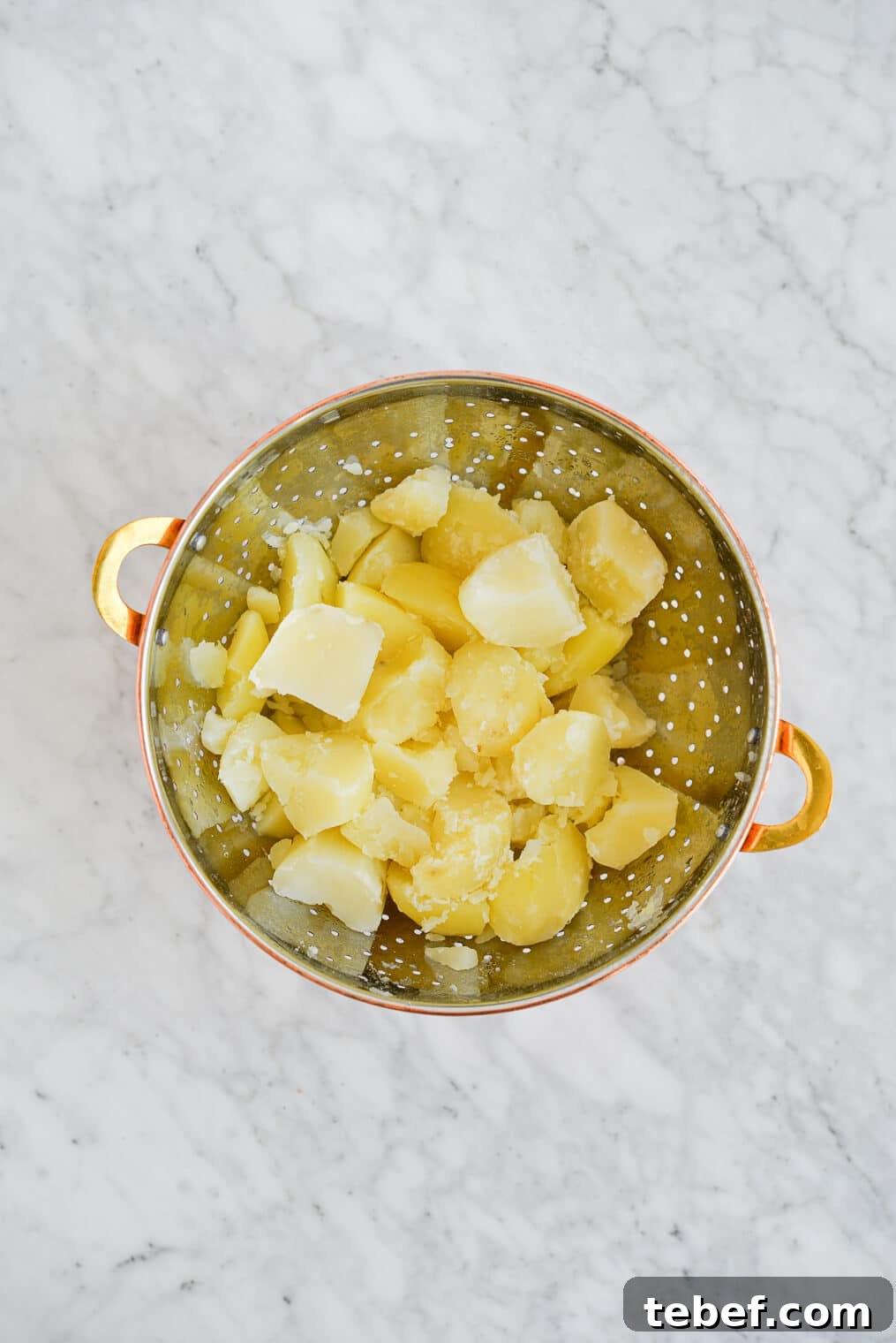 Ultra-Creamy Mashed Potatoes Recipe for Perfect Texture 5 chopped and boiled potatoes in a strainer on a marble surface