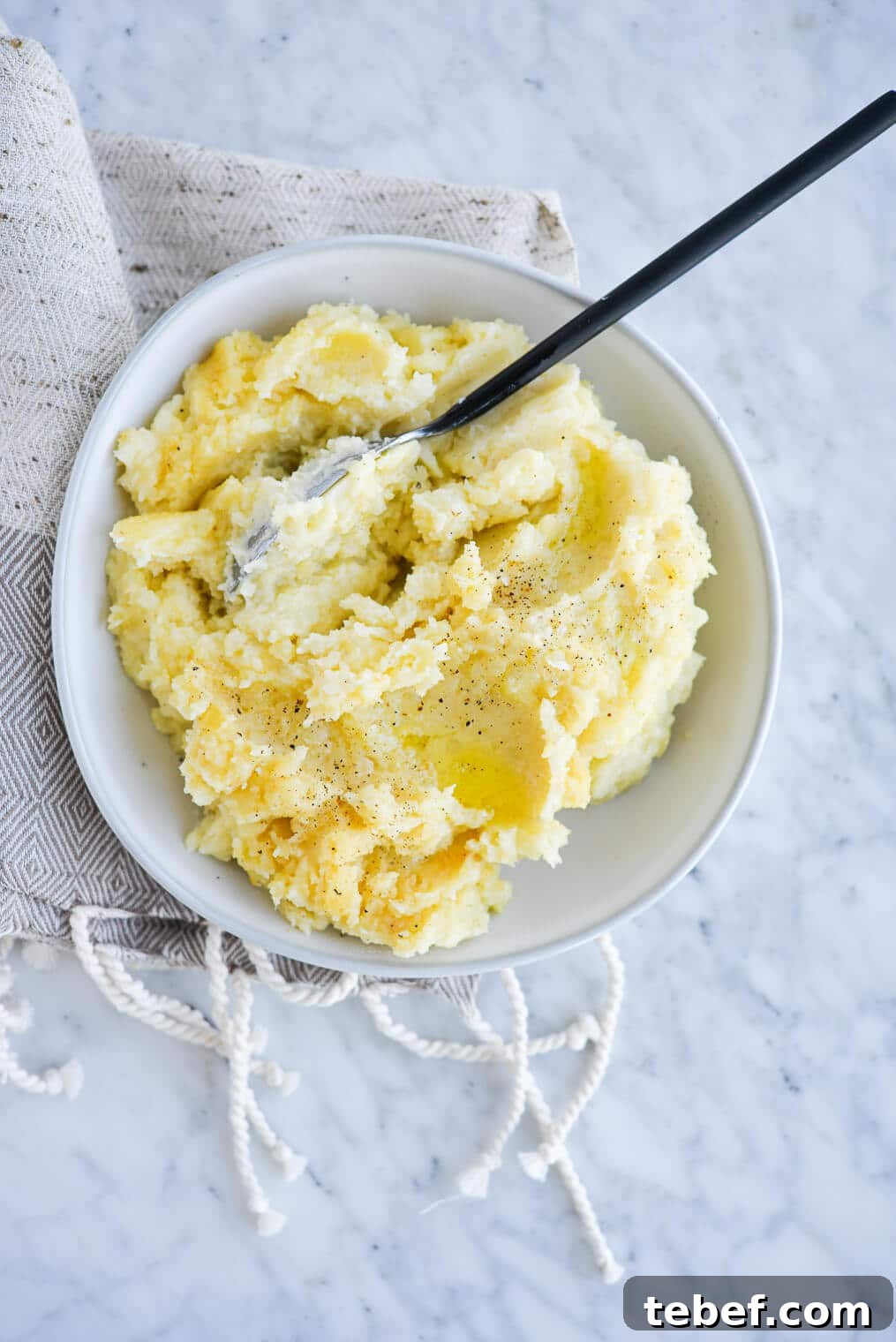 Ultra-Creamy Mashed Potatoes Recipe for Perfect Texture 8 top view of a bowl of ready-to-eat mashed potatoes with a serving spoon sitting on a marble surface
