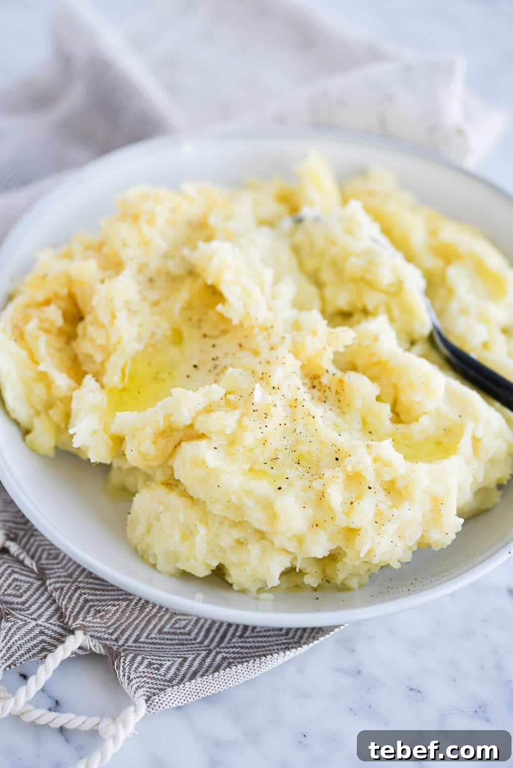 Ultra-Creamy Mashed Potatoes Recipe for Perfect Texture 9 side view of a bowl of mashed potatoes sitting on a marble surface
