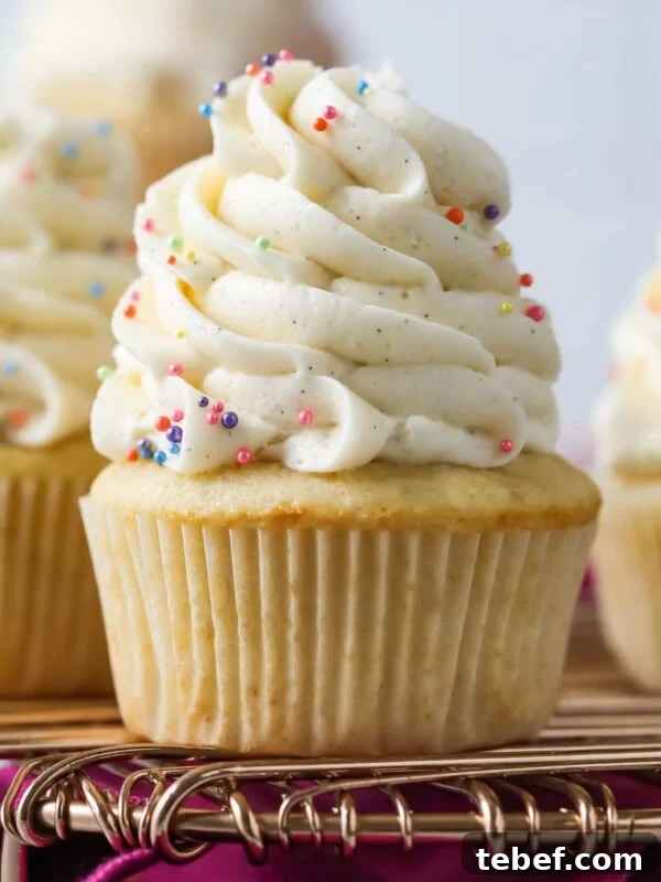 Vanilla cupcakes topped with tall swirls of vanilla bean buttercream on a cooling rack.