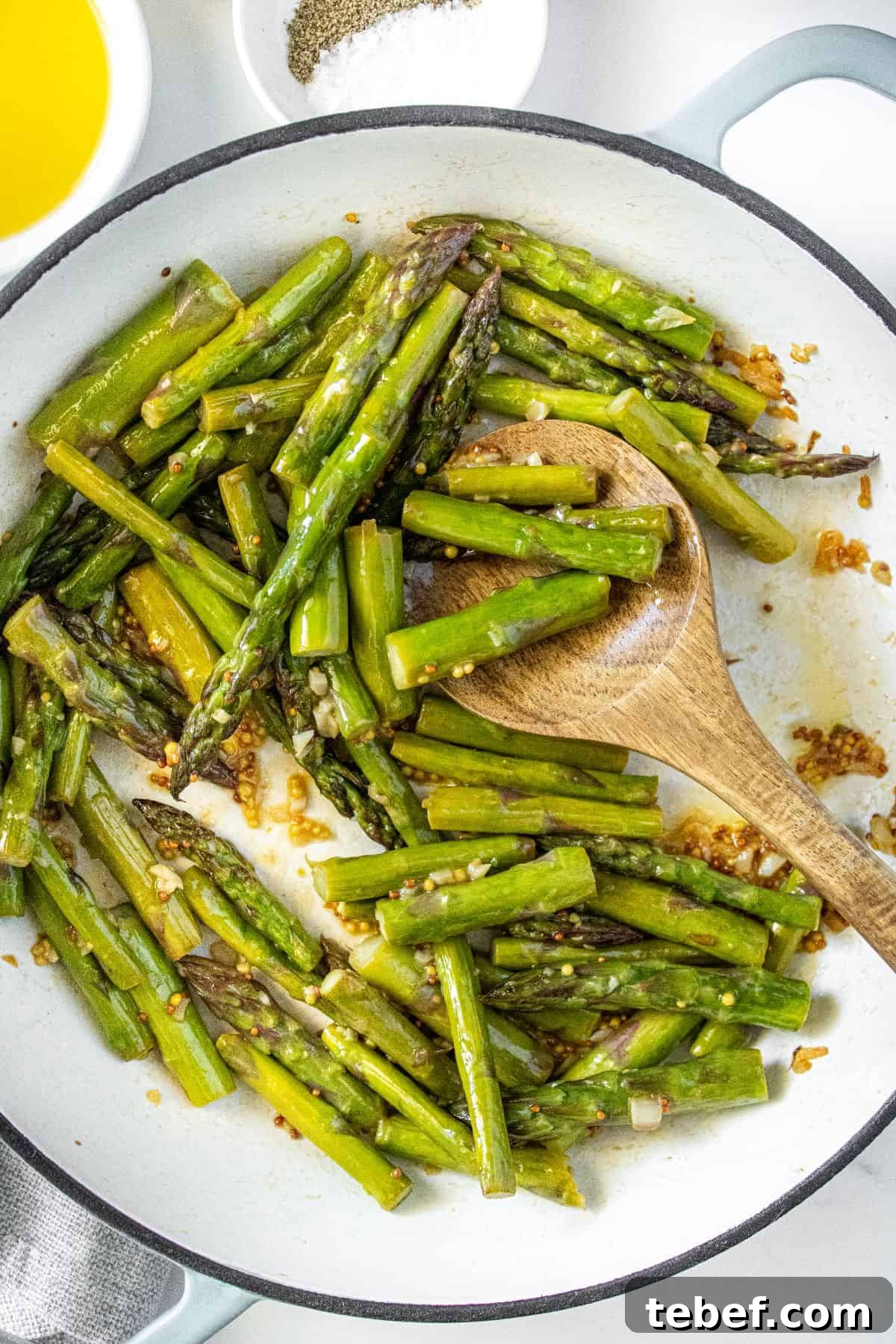 Crispy Garlic Sautéed Asparagus Recipe 2 Large frying pan with Sautéed Asparagus, and a wooden spoon resting in pan.