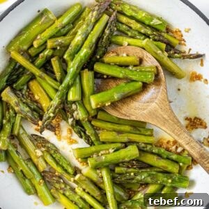 Crispy Garlic Sautéed Asparagus Recipe 11 Large frying pan with Sautéed Asparagus, and a wooden spoon resting in pan.