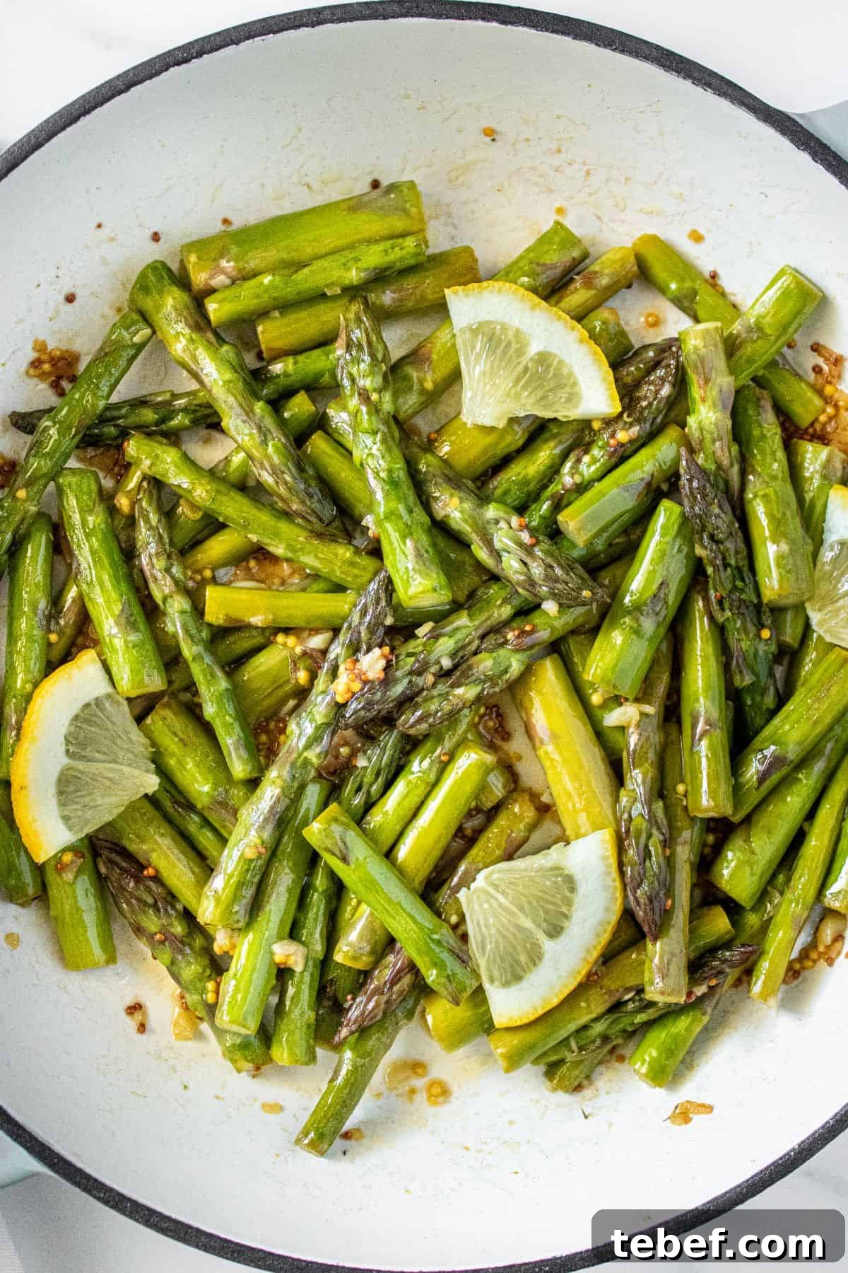 Crispy Garlic Sautéed Asparagus Recipe 6 Large frying pan with Sautéed Asparagus, garnished with some slices of lemon.