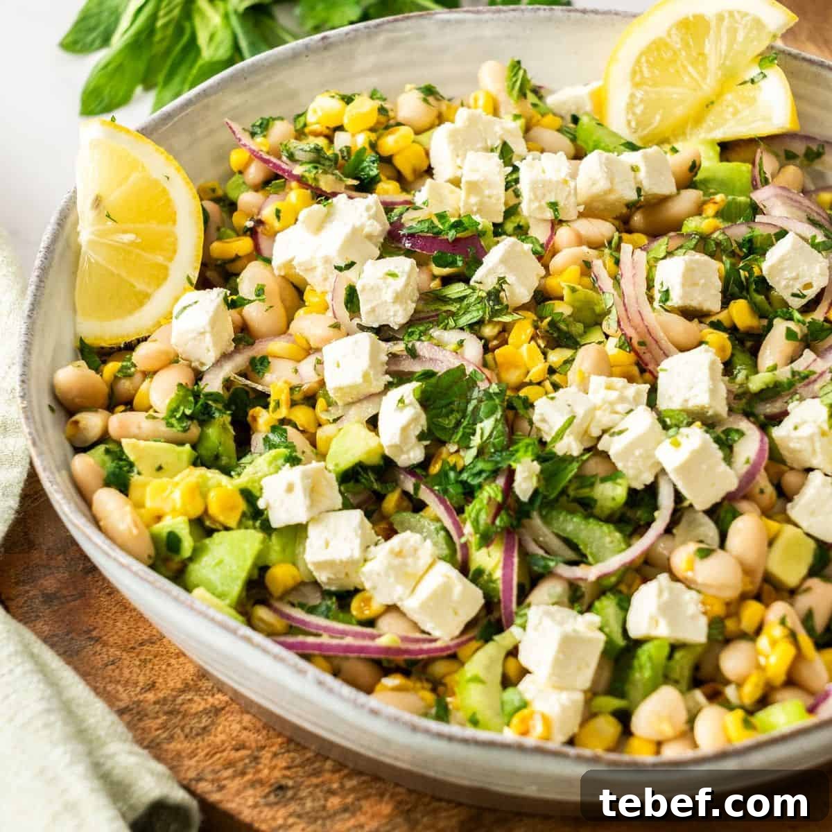 Round white bowl of Charred Corn Salad, with some lemon wedges on the side, sitting on a wooden board.